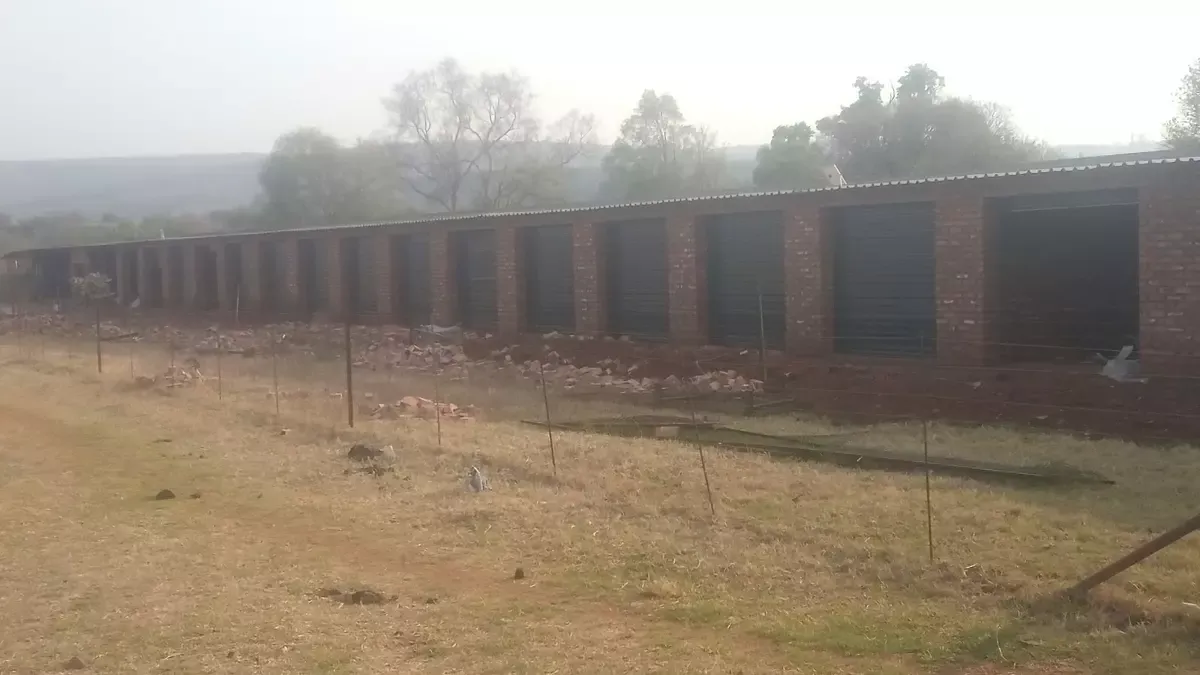 Row of brick storage units with dark doors behind a wire fence